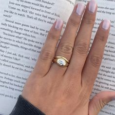 a woman's hand holding an open book with a ring on top of it