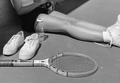 a woman sitting on the ground next to a tennis racket and bottle of water