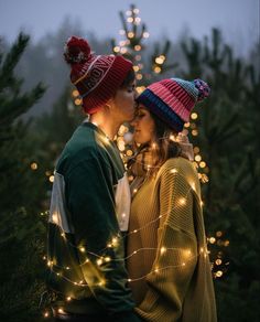 a man and woman standing next to each other in front of a christmas tree with lights