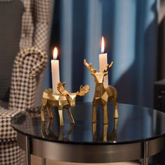 two gold deer candlesticks sitting on top of a glass table next to a chair