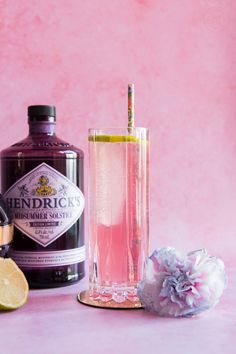 a bottle of gin and a glass with a lemon slice next to it on a pink background