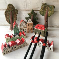 several small wooden houses and trees on a white table with paintbrushes in front of them