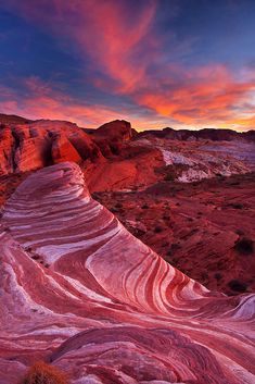 the desert is covered in red, white and blue rocks with waves on them at sunset