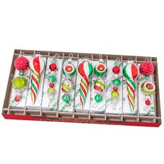 six christmas ornaments in a box on a white surface with red and green decorations around them