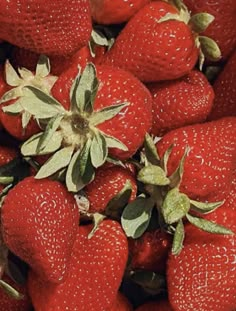 a pile of red strawberries with green leaves