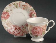 a white cup and saucer with pink flowers on it sitting next to a plate