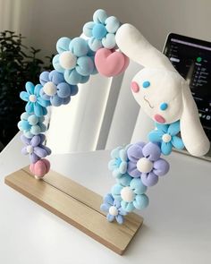 a stuffed animal sitting on top of a wooden stand next to a white table with blue and pink flowers