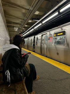 a person sitting on a bench looking at their cell phone next to a subway train