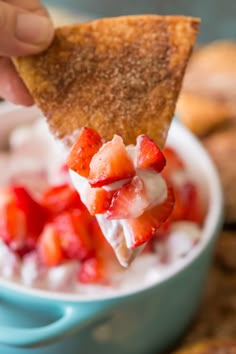 someone is dipping strawberries into a bowl of yogurt with crackers on the side