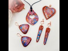 four pieces of jewelry sitting on top of a white table next to a pink rose