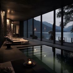 an indoor swimming pool in front of large windows overlooking the water and mountains at night