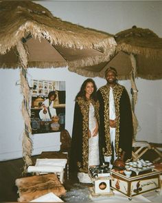 a man and woman standing next to each other in front of a bed covered with straw umbrellas