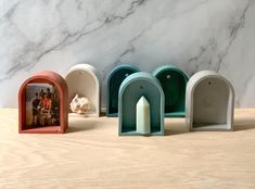 five small white and green arch shaped candlesticks on a wooden table next to a marble wall