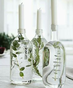 three bottles with plants in them sitting on a table next to two candles and plates