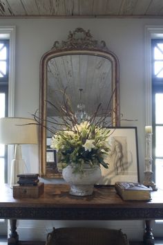 a vase filled with flowers sitting on top of a wooden table next to a mirror