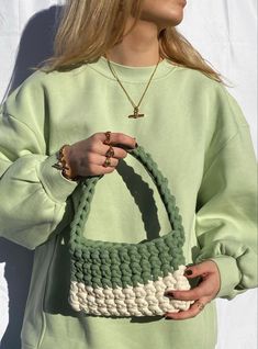 a woman wearing a green sweater holding a crocheted purse in front of her face