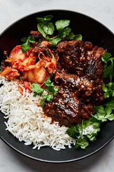 a black plate topped with rice and meat covered in sauce, garnished with cilantro