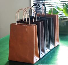 four brown and black shopping bags sitting on top of a green table next to a window