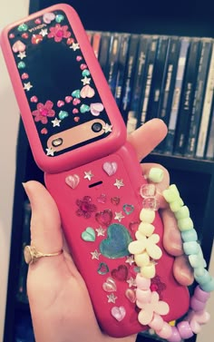 a person holding a pink cell phone with hearts and stars on the cover, in front of a bookcase