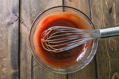 a whisk in a glass bowl filled with sauce on top of a wooden table