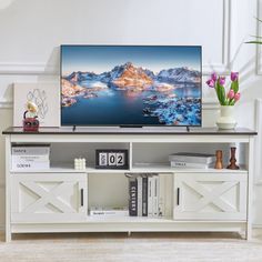 a flat screen tv sitting on top of a white entertainment center next to a vase with flowers