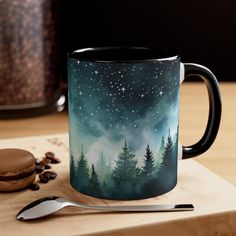 a coffee mug sitting on top of a wooden table next to a spoon and cookie