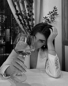 a woman sitting at a table with a glass of wine in front of her face