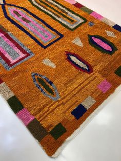 an orange rug with various colored shapes and lines on the top is laying on a white surface