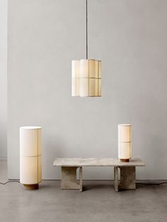 three lamps hanging from the ceiling next to a bench and table with a lamp on it