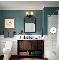 a white toilet sitting next to a bathroom sink under a mirror and light above it