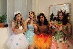 four women dressed in flowery dresses posing for a photo with one holding a potted plant