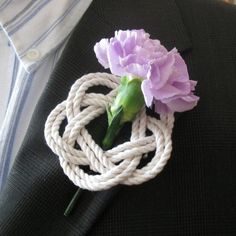 a purple flower sitting on top of a white piece of rope next to a black jacket