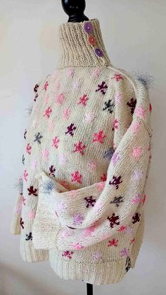 a white sweater with pink and purple flowers on the back, sitting on a mannequin's head