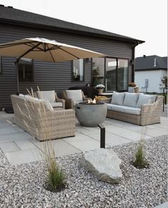 an outdoor living area with couches, chairs and an umbrella over the fire pit