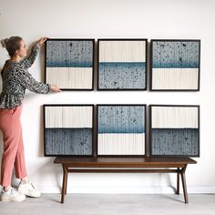 a woman standing next to four framed art pieces on a wall above a wooden bench