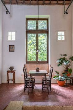 a dining table and chairs in front of a large window with potted plants on it