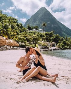 a man and woman sitting on the beach kissing