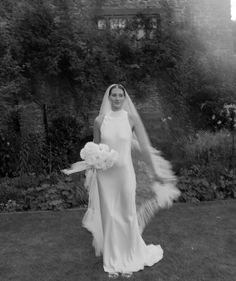 a woman in a wedding dress is walking through the grass with her veil blowing in the wind