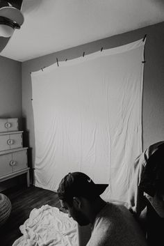 a man laying on top of a bed next to a white curtain in a bedroom