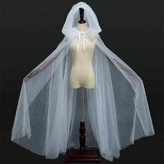 a mannequin wearing a white veil and dress on a wooden stand with black background