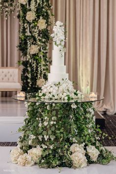 a wedding cake with white flowers and greenery on the top is surrounded by candles