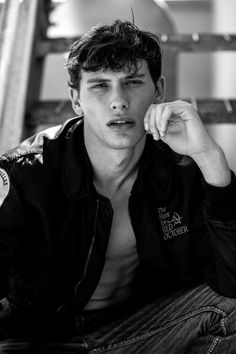 a young man sitting on the floor with his hand to his ear and looking at the camera