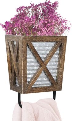 a wooden planter with purple flowers in it on a metal stand next to a pink towel