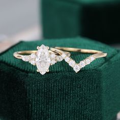 two engagement rings sitting on top of a green velvet ring box with white stones in the middle