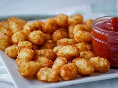 a white plate topped with tater tots next to a jar of ketchup