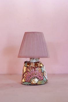 a lamp with a pink shade on it sitting next to a pink wall and floor