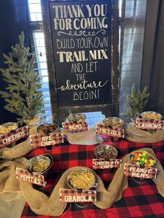 a table topped with bowls filled with food next to a sign that says thank you for coming build your own trail mix and let the adventure begin