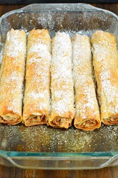 some food that is in a glass dish on a wooden table and covered with powdered sugar