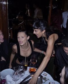 people sitting at a table with wine glasses in front of them and one woman smiling