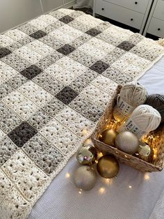 a crocheted blanket and balls of yarn on a bed with christmas lights in front of it